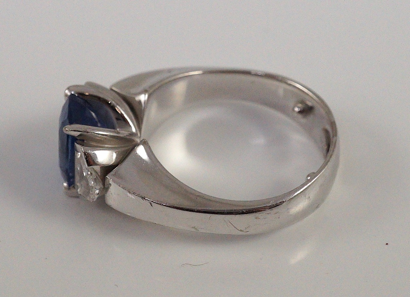 A modern white gold (tests as 18ct), single stone oval cut Ceylon sapphire and two stone shield cut diamond set dress ring, by Musson